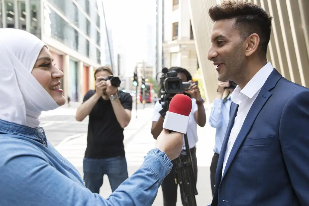 Journalist interviewing a businessman outdoors with photographers recording the moment